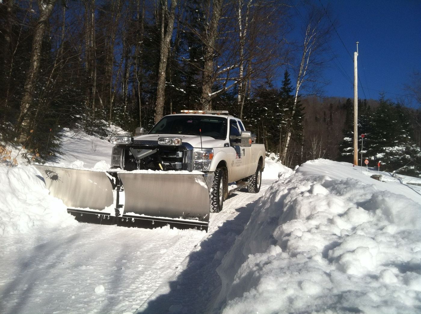 White Burgess plow truck clearing a deep snowbank on a wooded road