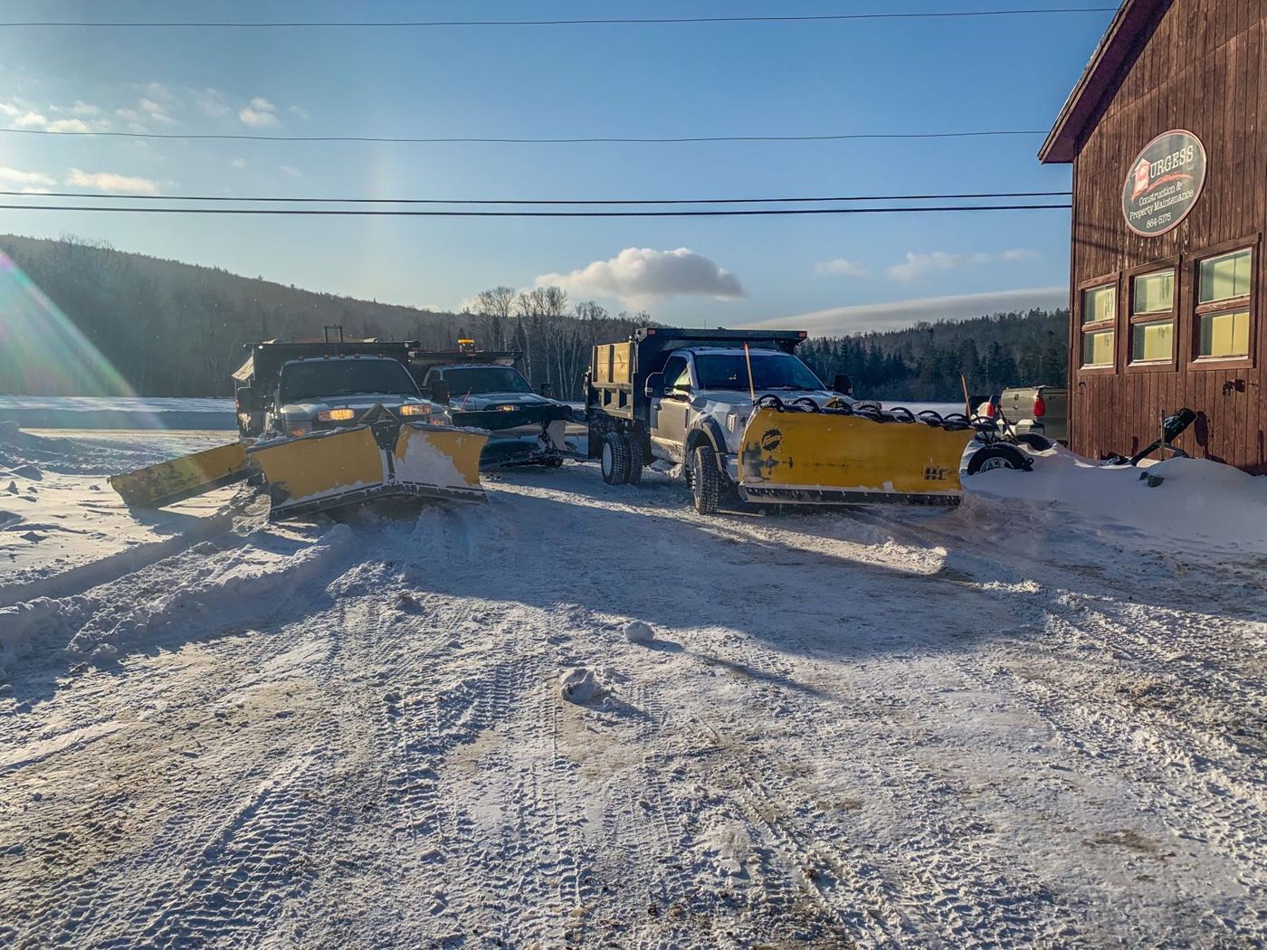 Burgess plow trucks lined up outside the shop with the Burgess Construction & Property Maintenance sign