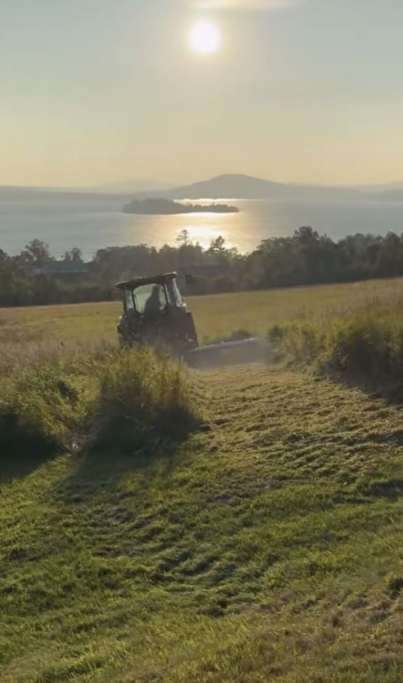 Tractor mowing a hillside field above Rangeley Lake at sunset