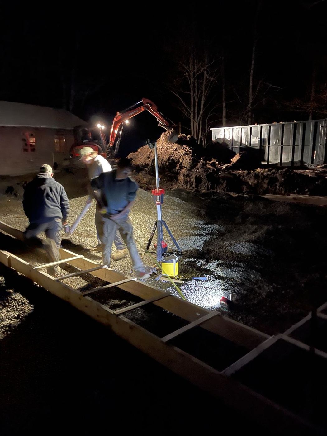 Crew setting footing forms at night under work lights