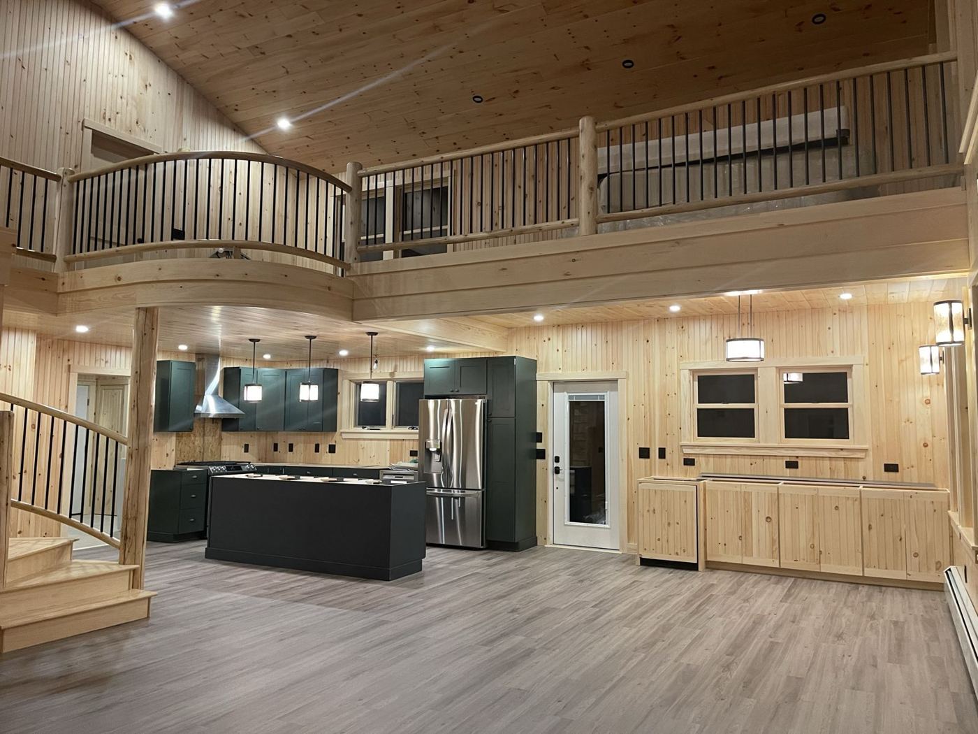 The new great room: pine walls, curved balcony, log posts and a kitchen with green cabinets