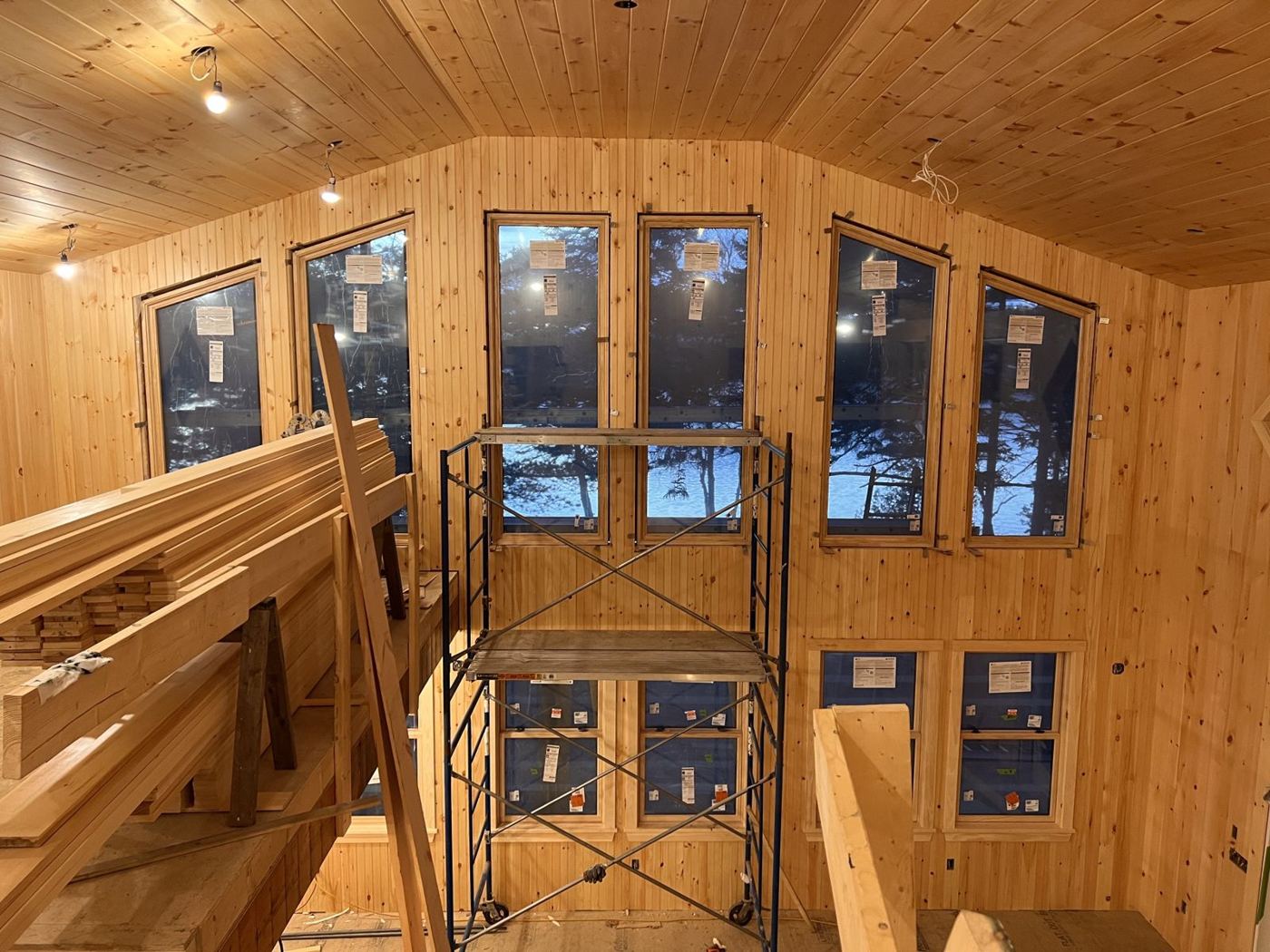 Wall of tall windows in the pine-lined great room, looking out to the lake