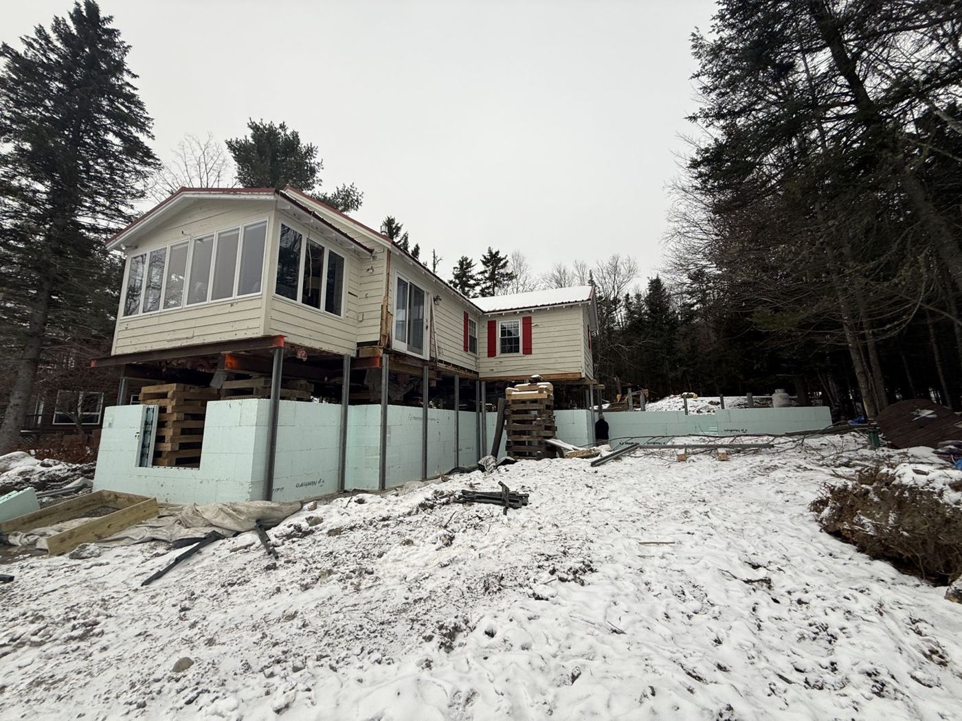 Red-shuttered lakeside camp raised on steel, with ICF walls going in below