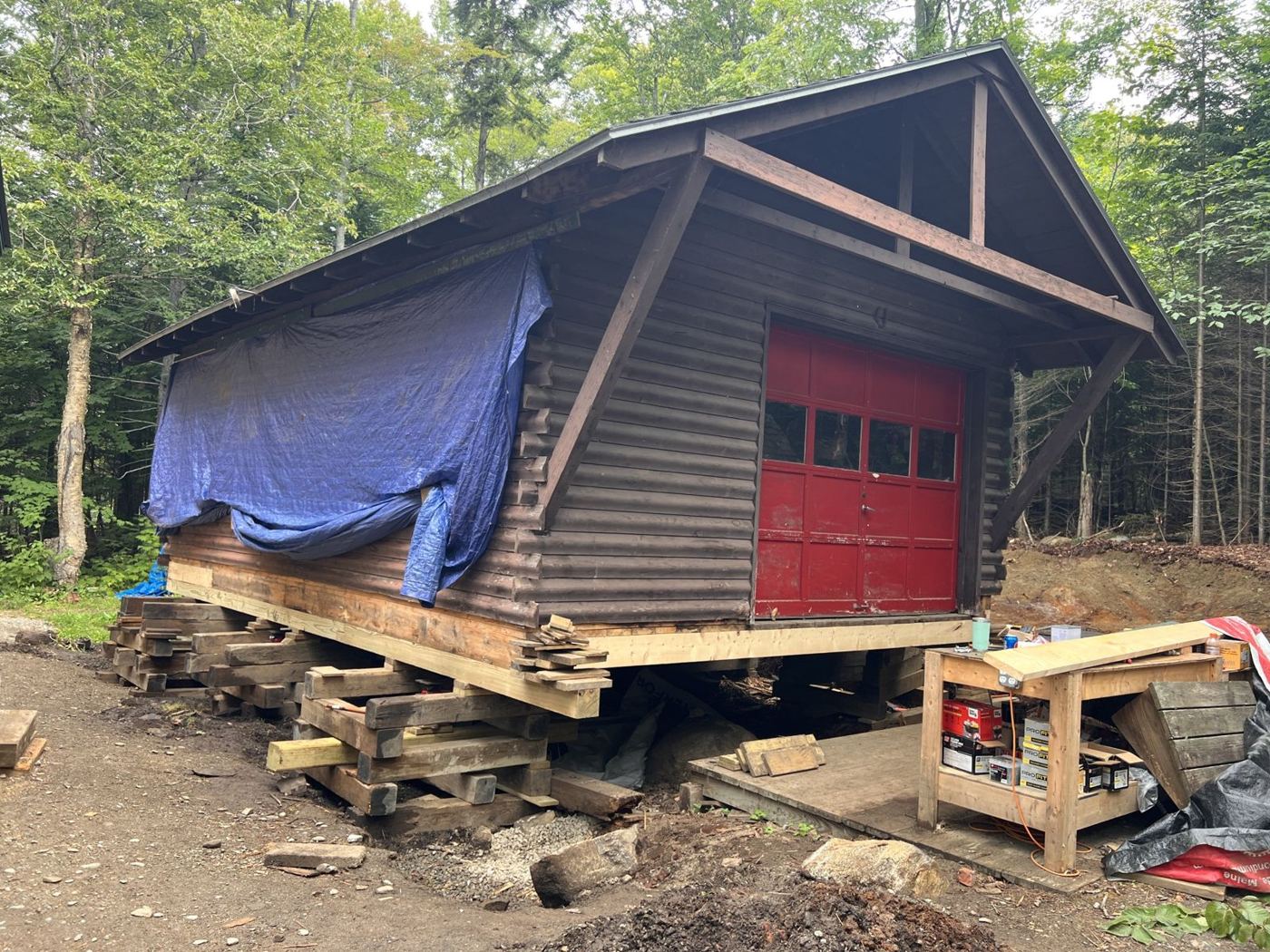 Log garage with a red door lifted on timber cribbing