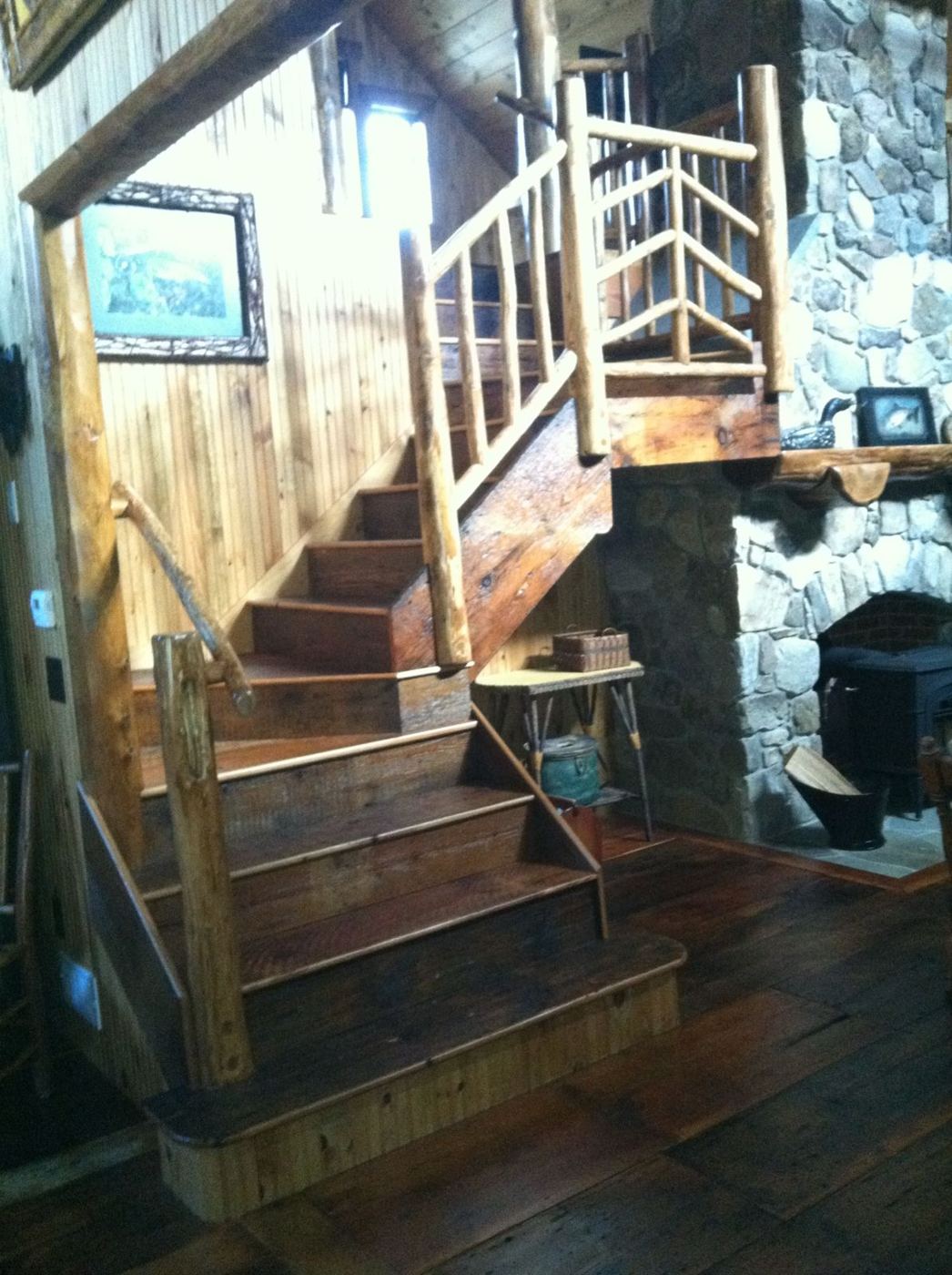 Finished staircase with peeled-log railings beside the stone fireplace and wood stove