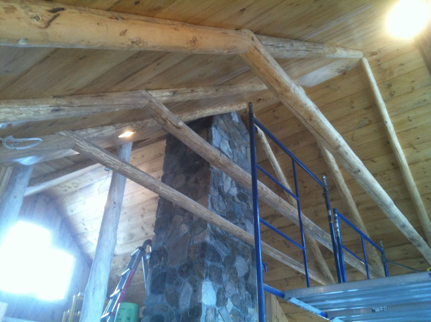 Log trusses and pine ceiling around a tall stone chimney