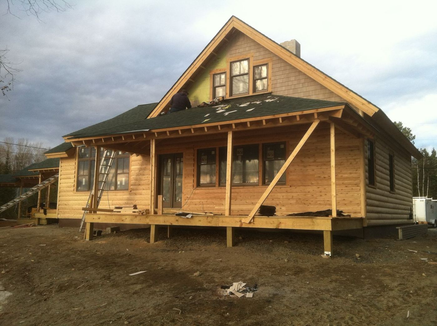 The new home with fresh log siding, shingled gable and porch roof being finished